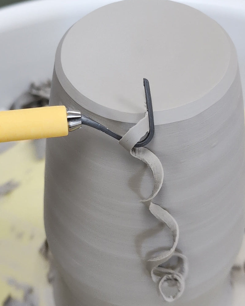 Lemon hook trimming tool pulling a long spiral ribbon of clay off a pot